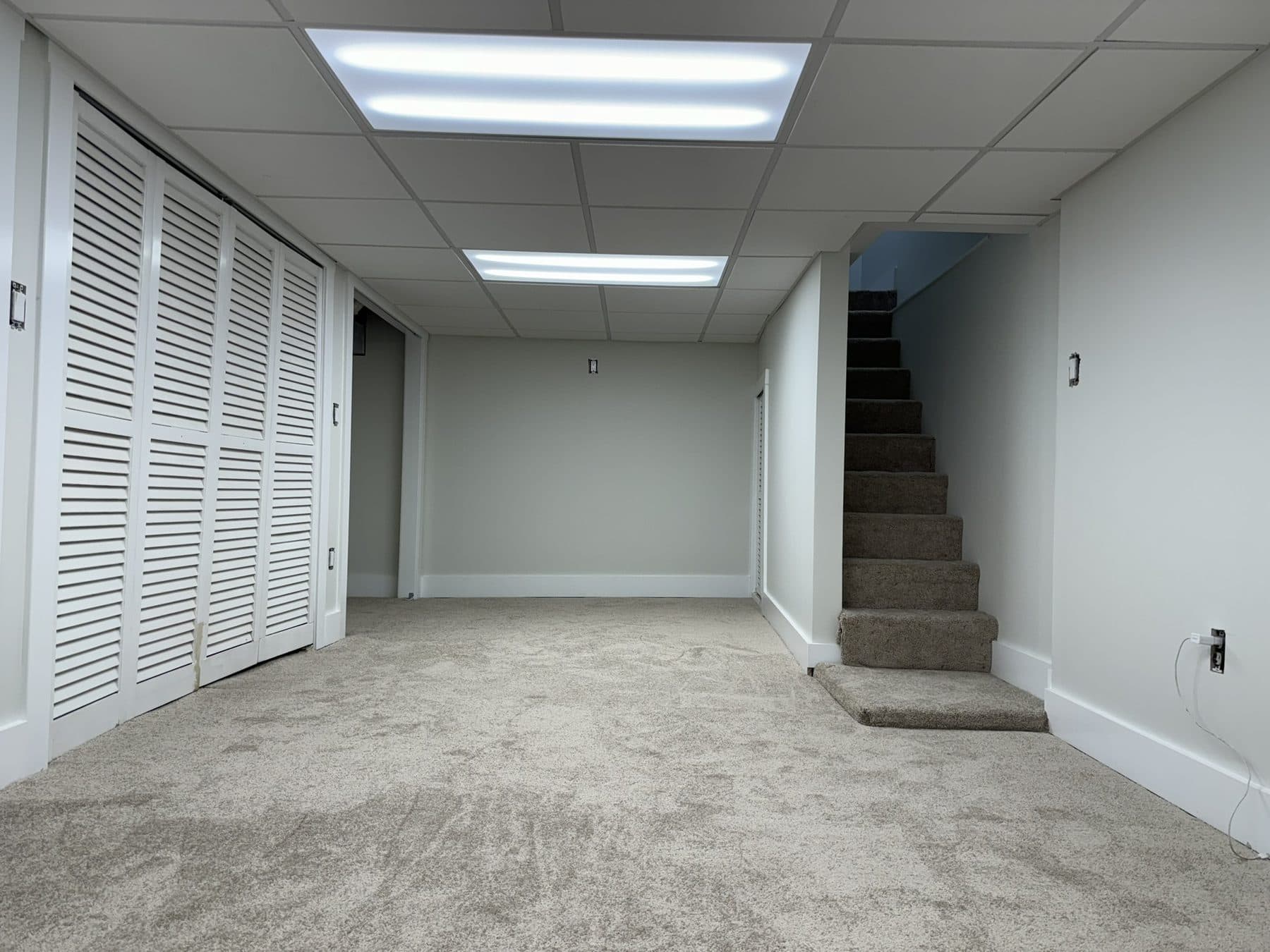 Finished basement with carpet, louvered closet doors and a drop ceiling